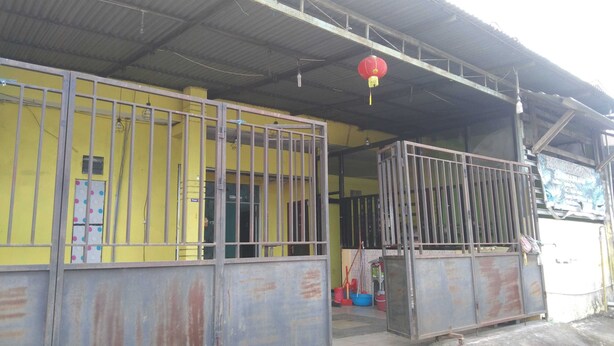 A building with yellow walls and metal gates, a red lantern hanging from the roof, and a sign that reads "KOSTUM HOUSE". - EXPRESS O 91281 Guest House Indah Jaya (Tarakan)