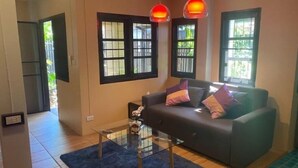 A living room with a sofa, two pendant lights, a glass coffee table, and a blue rug.