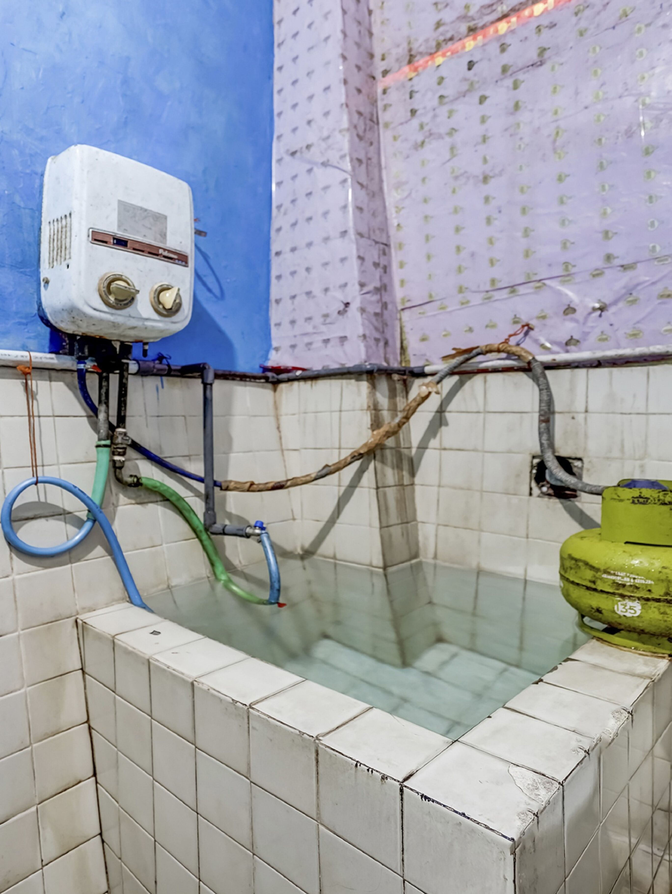 Un baño con una bañera, un calentador blanco y un cilindro de gas verde.