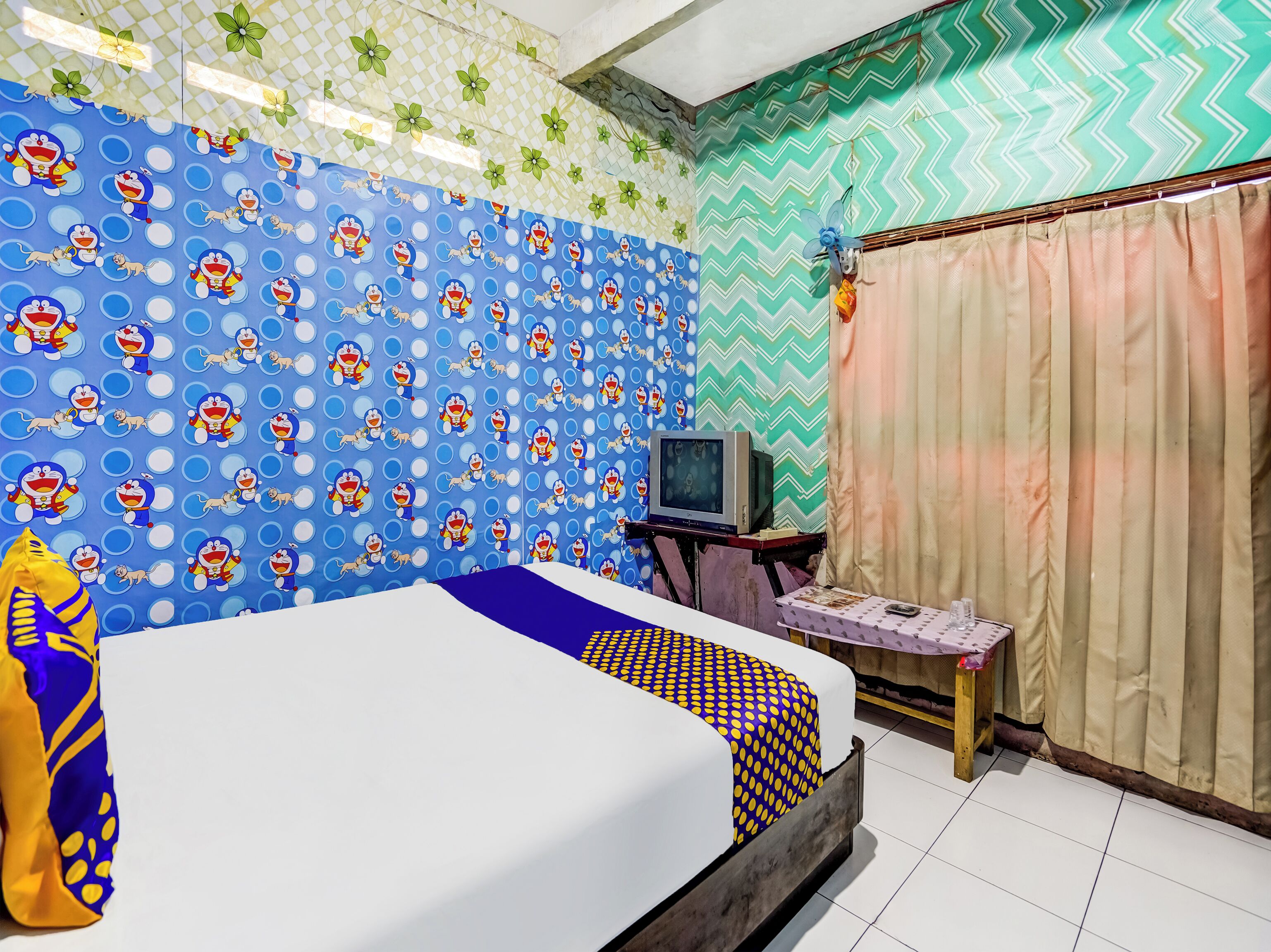 Une pièce avec un lit, un téléviseur posé sur un meuble en bois et des murs à motifs.