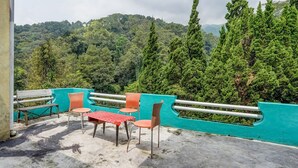 A terrace with a table and chairs, a view of a forested hill, and a turquoise wall. - OYO Life 91060 Villa Wijaya Homestay (Prigen)