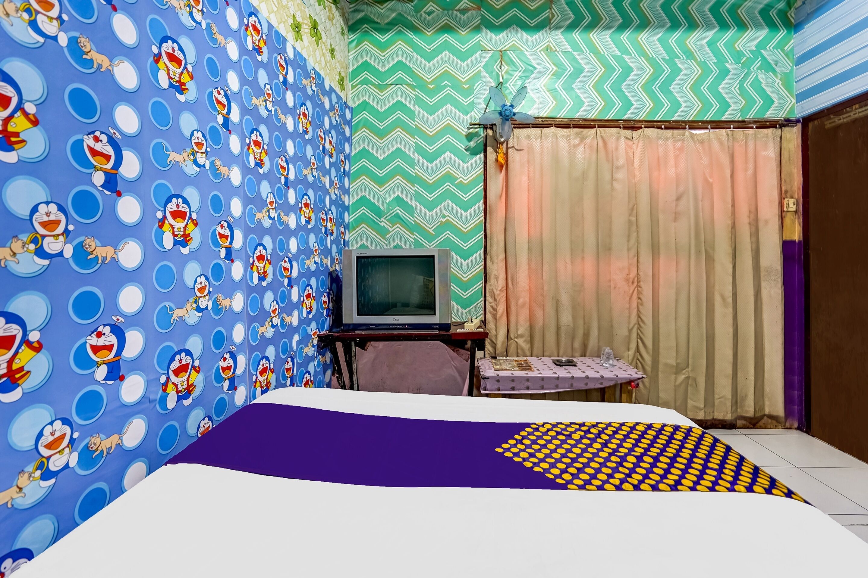 Una habitación con una cama, un televisor sobre un soporte y una mesita con un vaso.