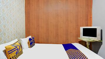 A hotel room with a wooden headboard, a bed with patterned pillows, a TV on a wooden stand, and a patterned wall.