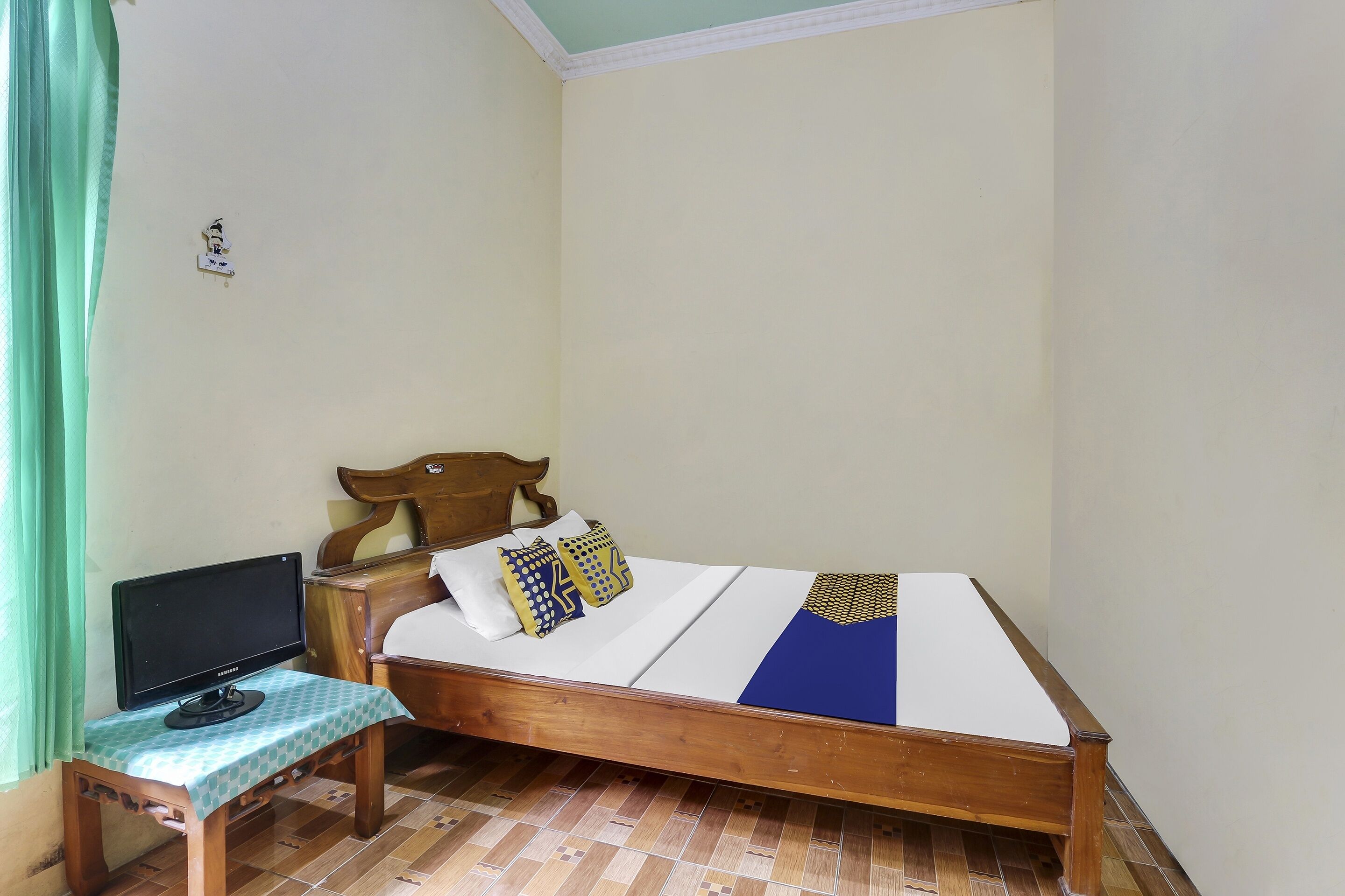 Un letto singolo con una testiera in legno, un comodino con un monitor e una tenda verde.