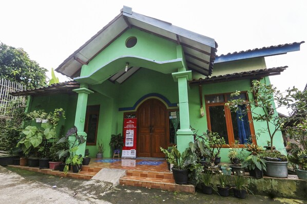 A green building with a wooden door, potted plants, and a tiled entrance. - OYO Homes 91151 Desa Wisata Kreatif Perdamaian Srumbung Gunung (Bawen)