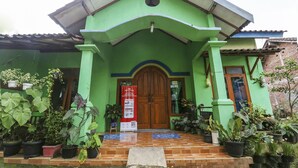 A green building with a wooden door, potted plants, and a tiled entrance. - OYO Homes 91151 Desa Wisata Kreatif Perdamaian Srumbung Gunung (Bawen)