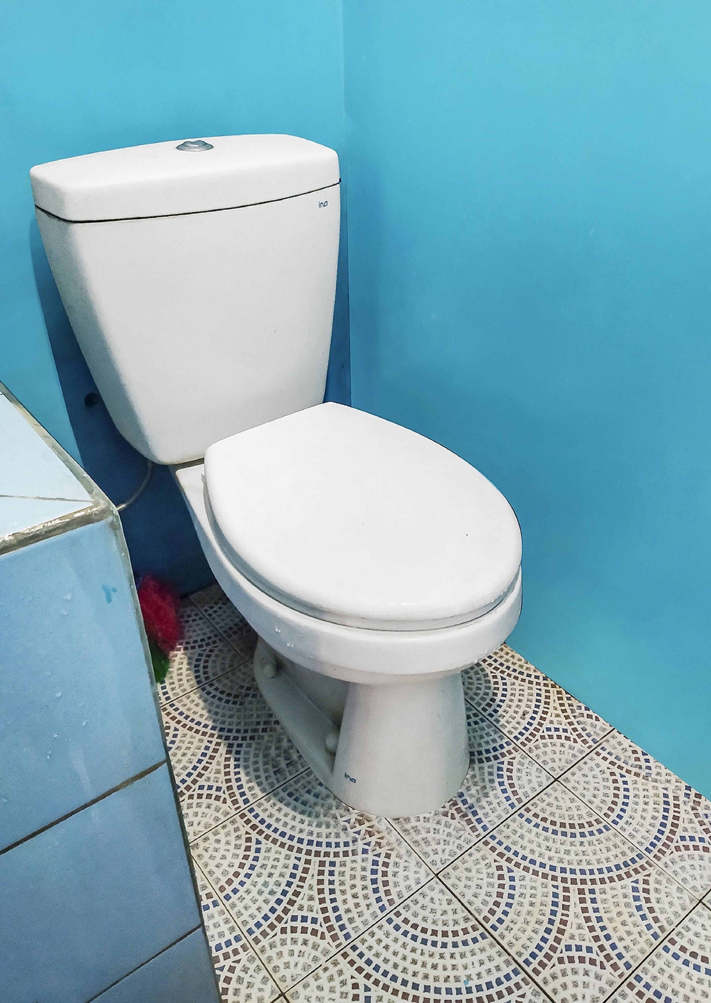 A toilet with a white seat and lid, a blue wall, and a patterned floor.