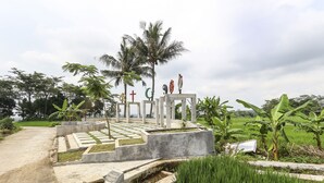 A garden with a pathway leading to a structure with religious symbols. - OYO Homes 91151 Desa Wisata Kreatif Perdamaian Srumbung Gunung (Bawen)