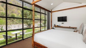 Una habitación con una cama grande, un televisor en la pared y vistas a un paisaje natural a través de amplias ventanas.