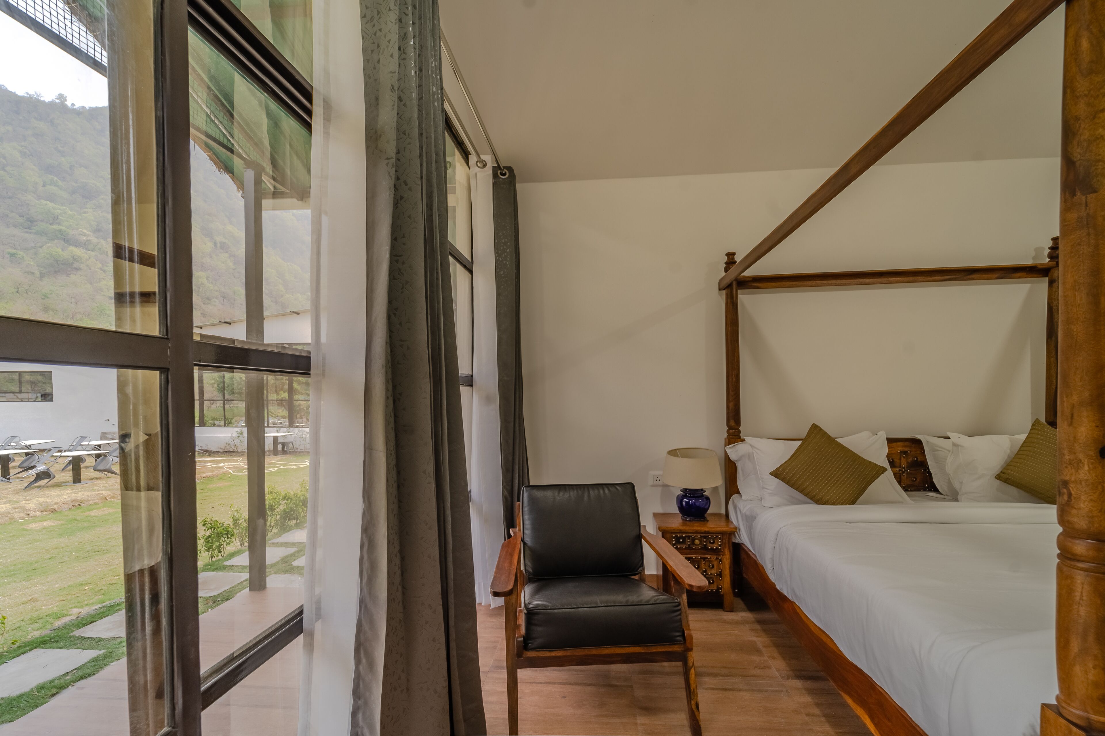 A four-poster bed with a wooden frame, a small wooden nightstand with a lamp, and a chair.