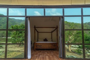 A room with a four-poster bed, large windows, and a view of a forested landscape.