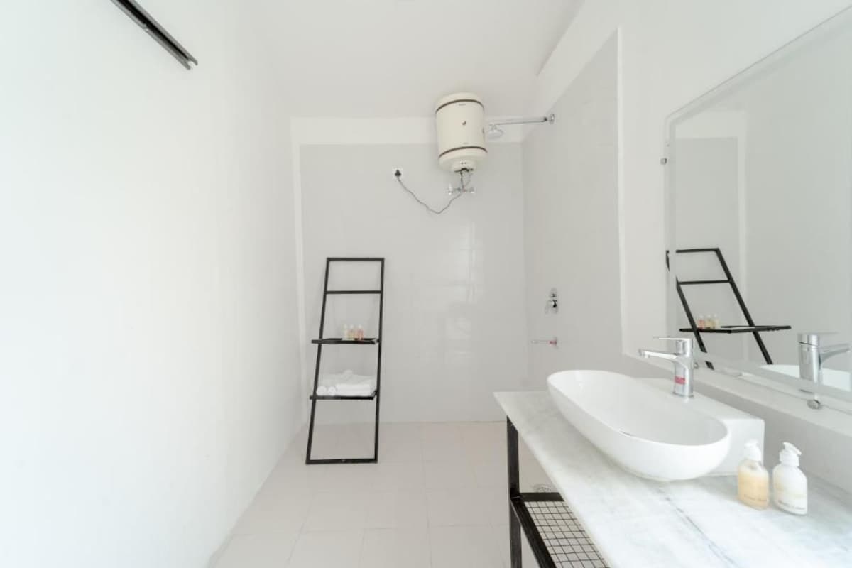 Un baño moderno con un lavamanos blanco, un espejo grande y una estantería negra.