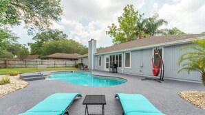 A backyard with a swimming pool, two lounge chairs, a covered table, and a red hanging chair. - *True Blue Pool Oasis* ping-pong, wi-fi, tv (Jacksonville)