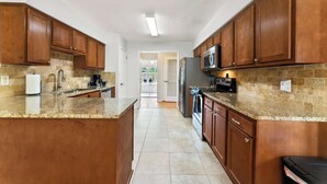 A kitchen with wooden cabinets, a granite countertop, a stainless steel refrigerator, and a microwave. - *True Blue Pool Oasis* ping-pong, wi-fi, tv (Jacksonville)