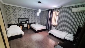 A hotel room with three beds, a desk, and a chair. There is a window with curtains and an air conditioning unit on the wall. - chveni sakhli (Tbilisi)