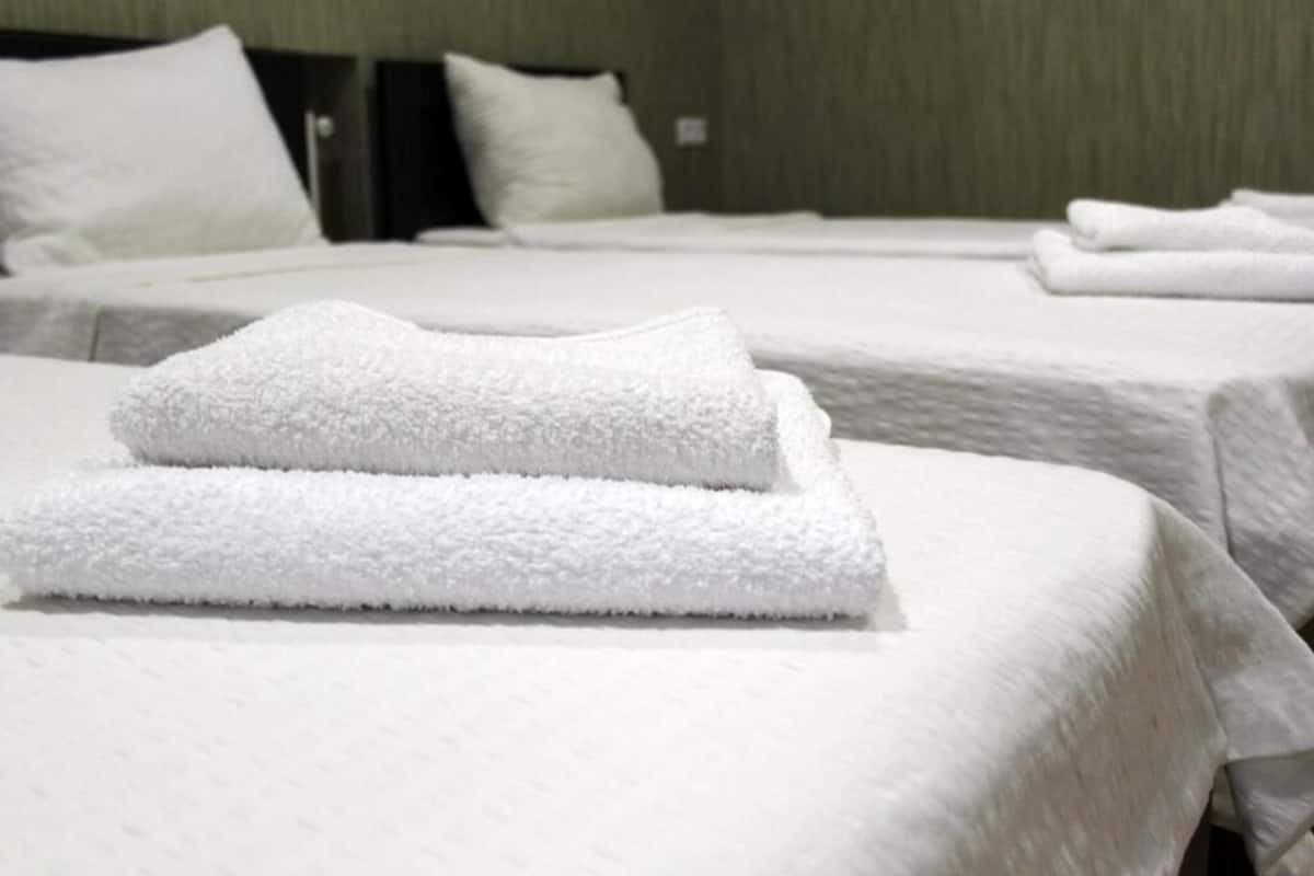 Ein Hotelzimmer mit ordentlich bezogenen Betten, jedes mit weißen Leinentüchern und Kissen.