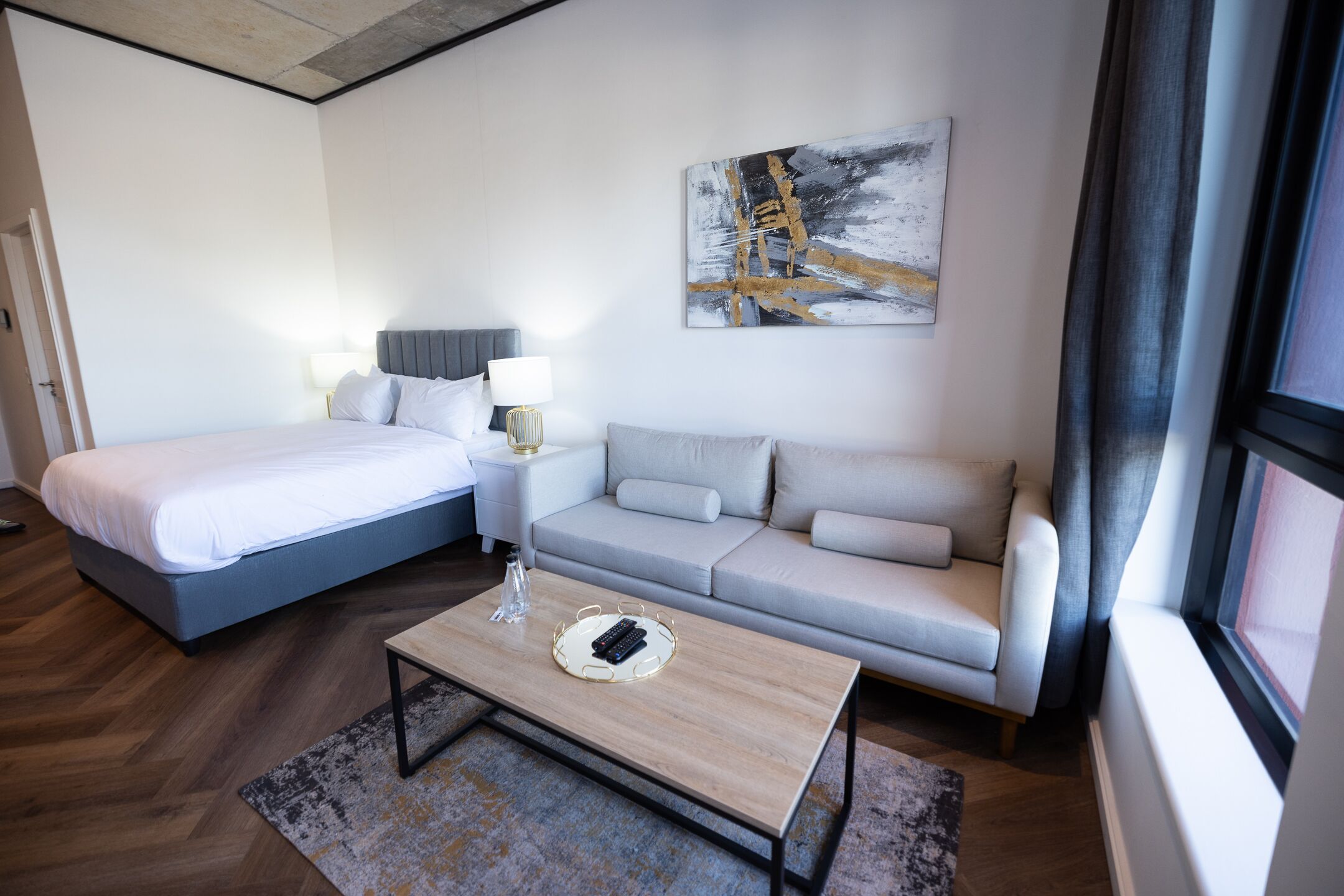 A hotel room with a bed, a sofa, a coffee table, and a painting on the wall.