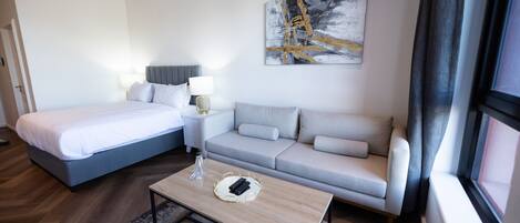 A hotel room with a bed, a sofa, a coffee table, and a painting on the wall.