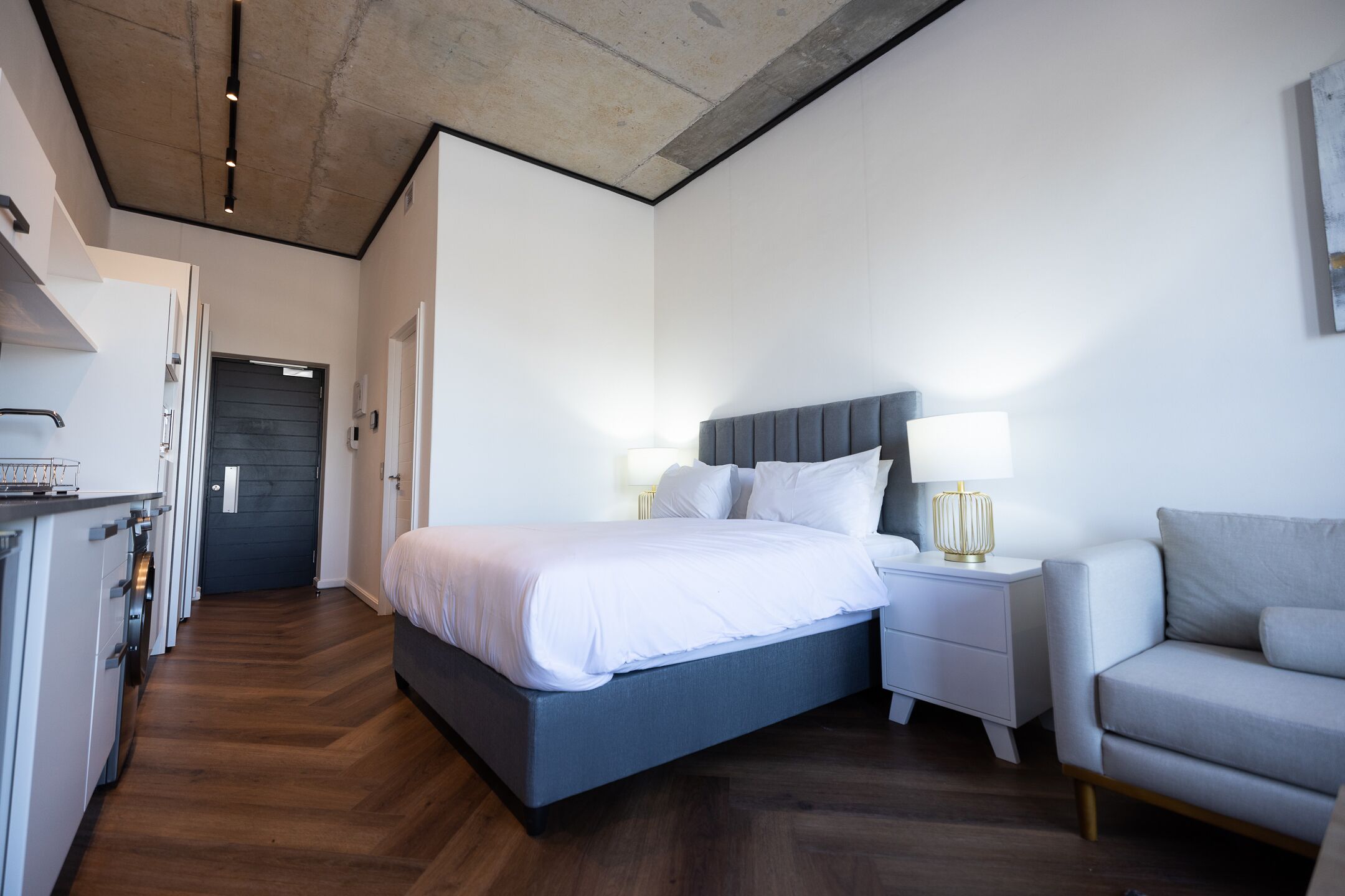 Una habitación de hotel moderna con una cama grande, mesitas de noche, un sofá y una zona de cocina.
