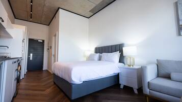 Una habitación de hotel moderna con una cama grande, mesitas de noche, un sofá y una zona de cocina.
