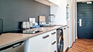 A modern kitchen with white cabinetry, a stainless steel range hood, a built-in dishwasher, and a wooden floor.