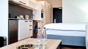 A modern hotel room with a wooden table, a bed, a washing machine, and a projector screen.