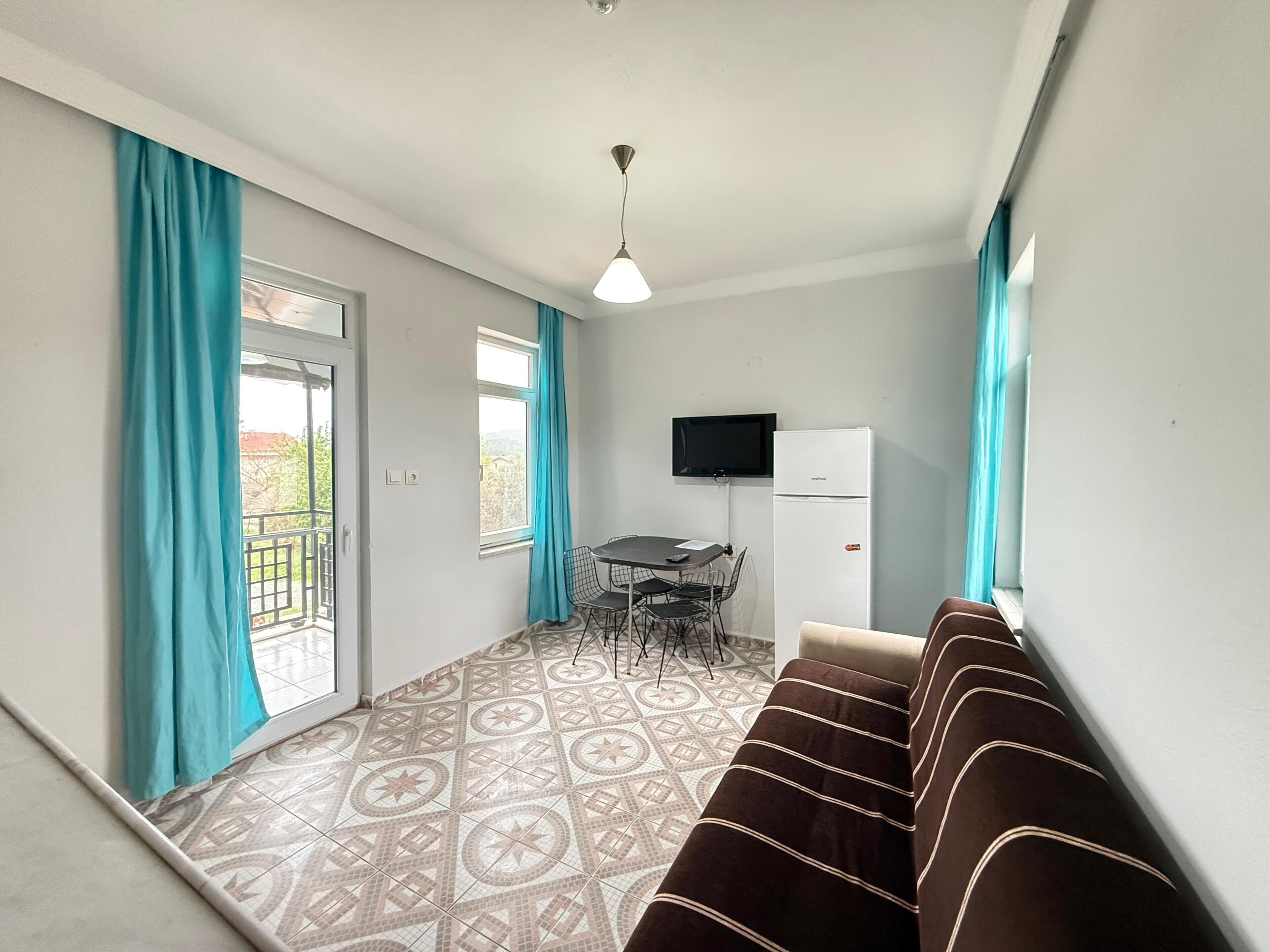 Una habitación con piso estampado, un sofá, una mesa con sillas, un televisor y un refrigerador.