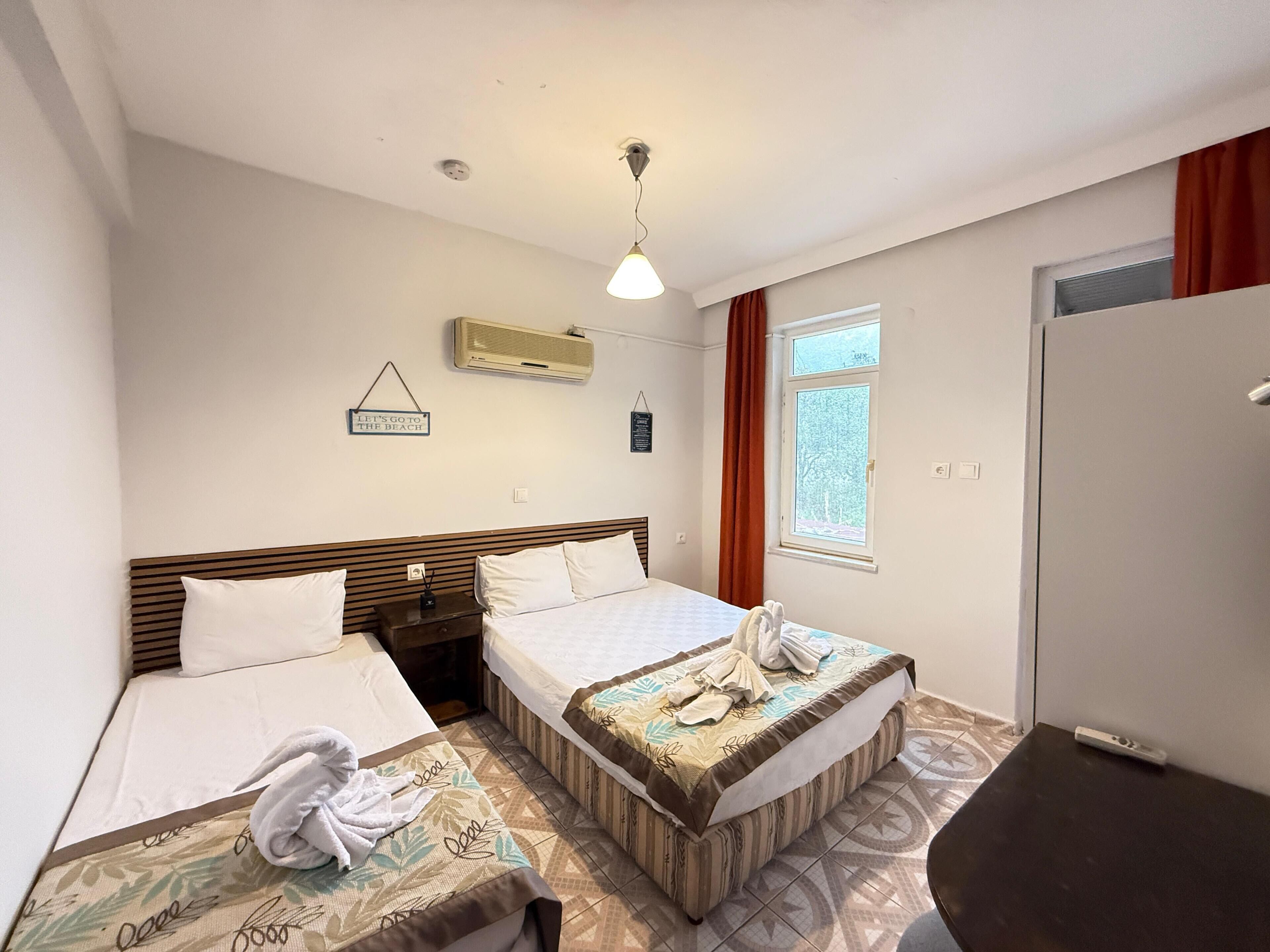 Habitación de hotel con dos camas, una ventana con cortinas, un equipo de aire acondicionado y un cartel en la pared.