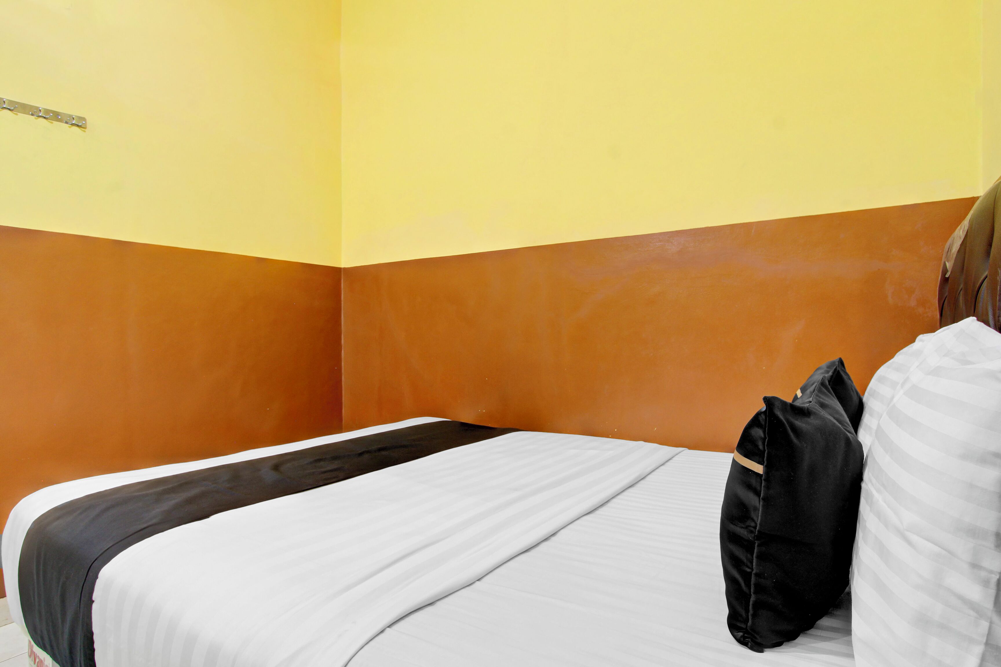 A single bed with a white and black bedspread, two pillows, and a wooden headboard.