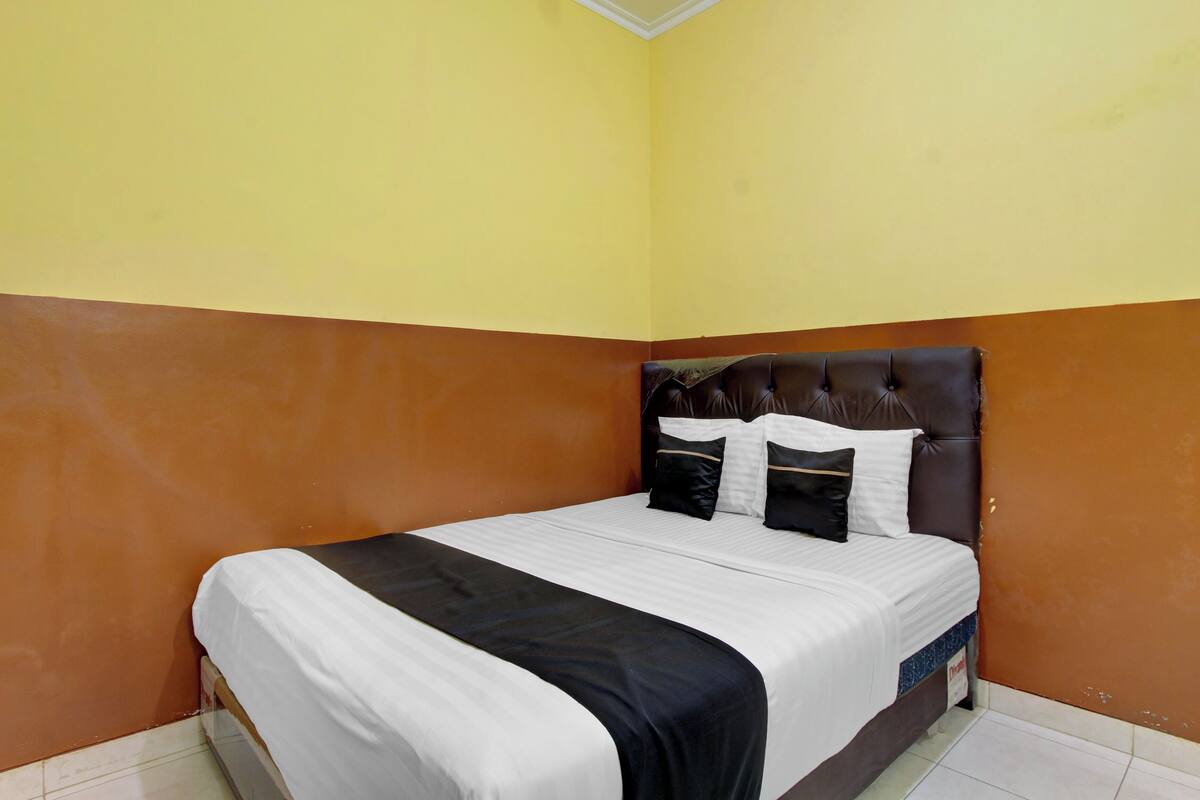 A single bed with a headboard, white bedding, and a black accent.