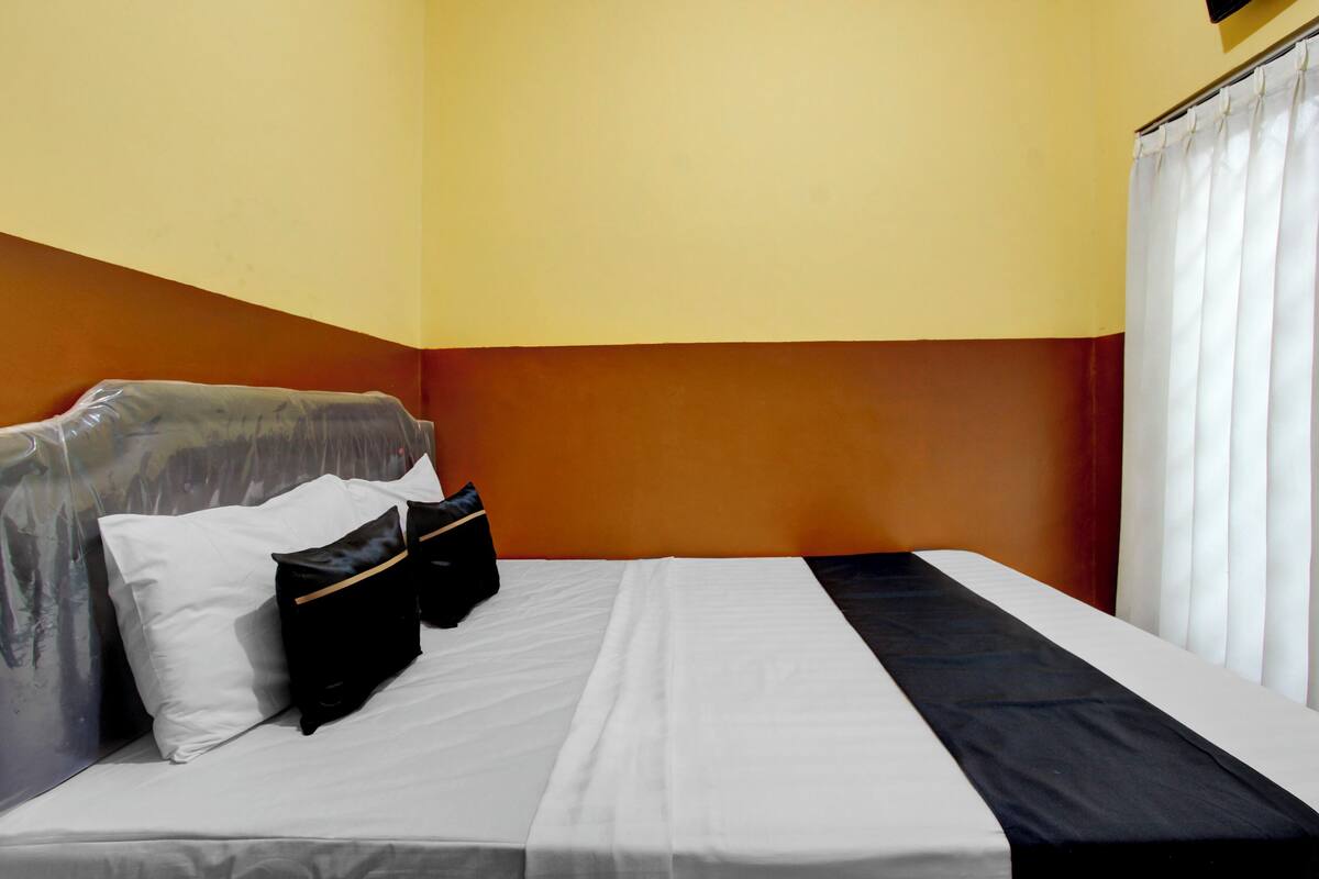 A hotel room with a bed, pillows, a black bag, and a window with curtains.