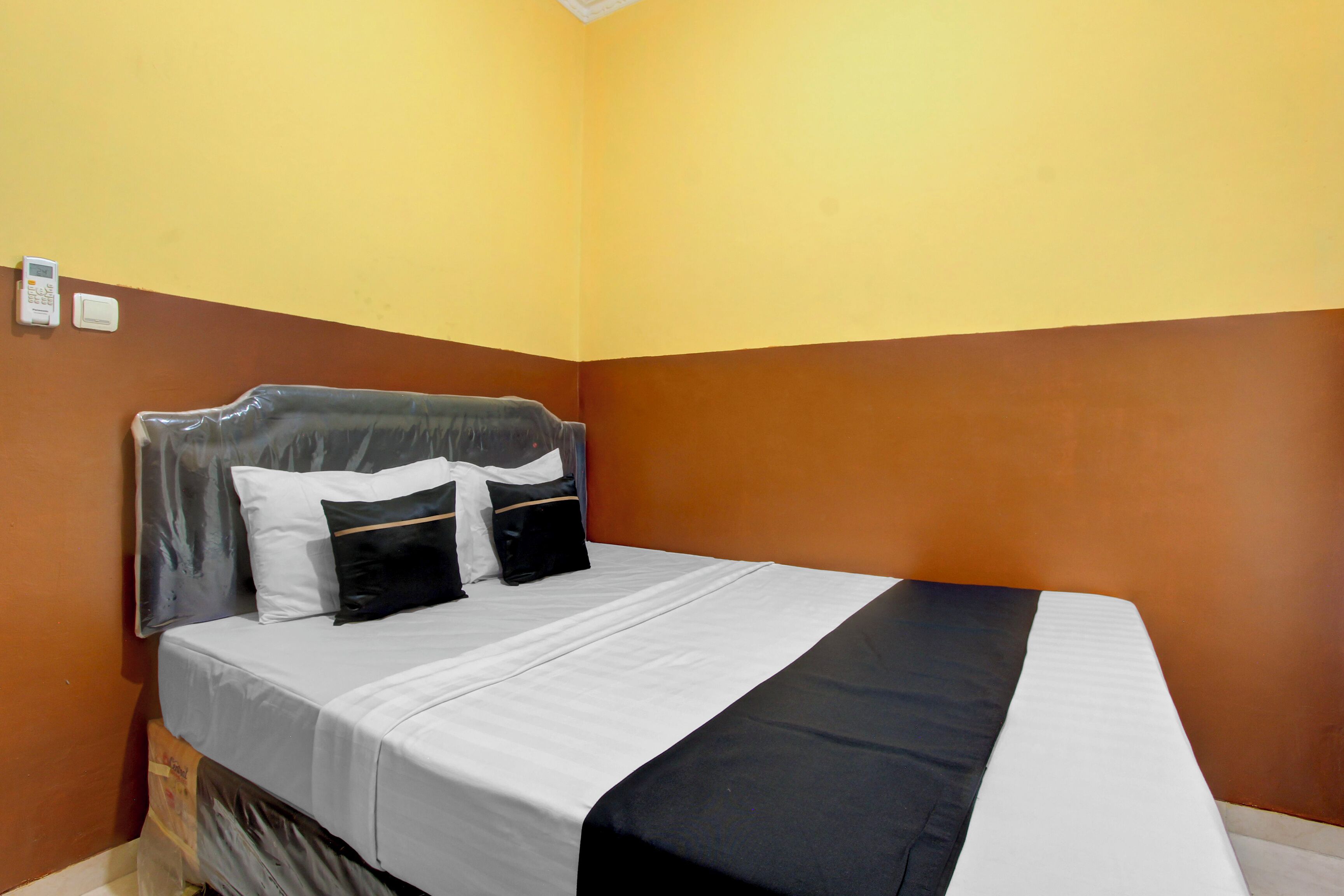 Een hotelkamer met een bed, kussens, een hoofdbord en een aan de muur bevestigde thermostaat.