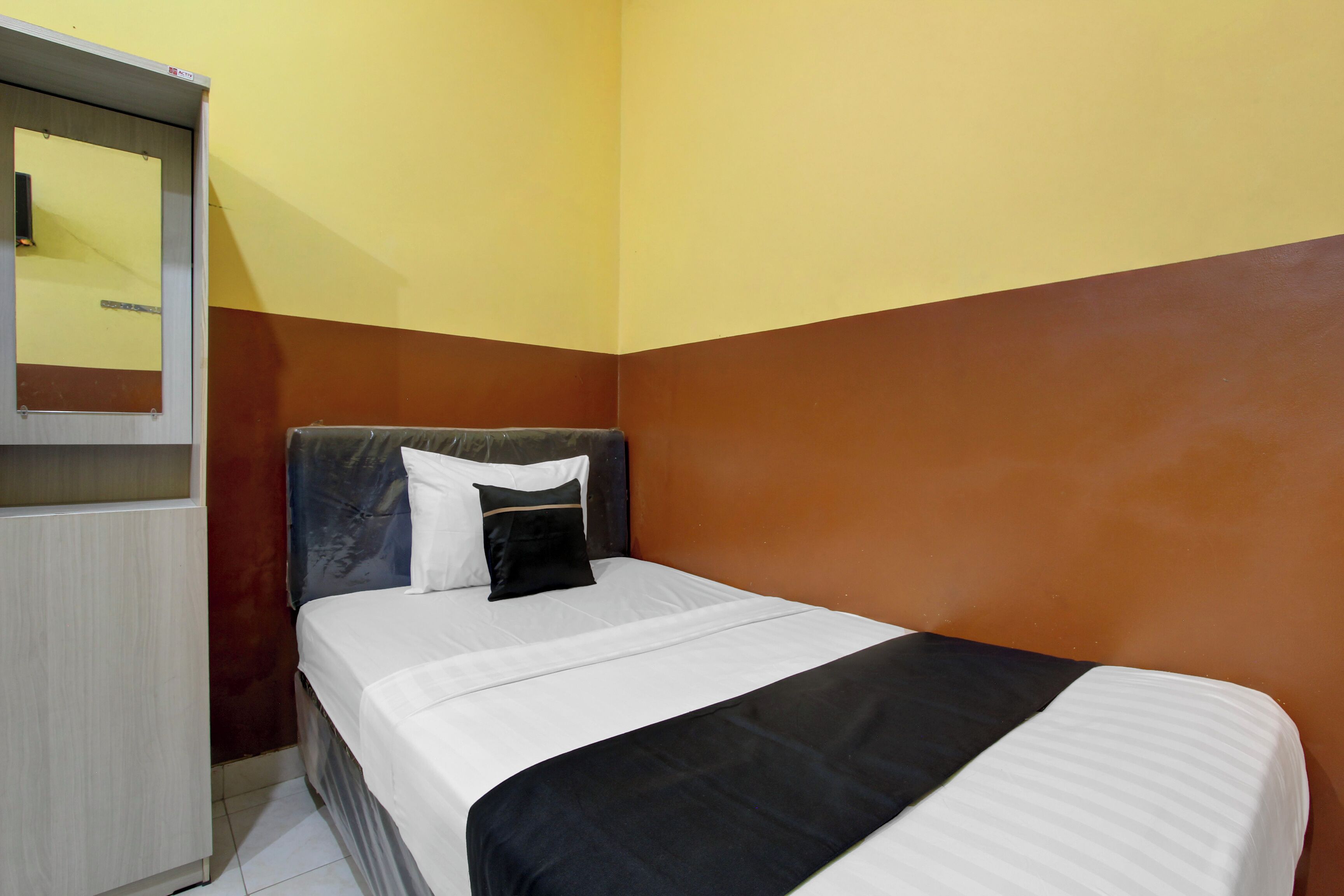 A single bed with white and black bedding, a wooden headboard, and a mirror on the wall.