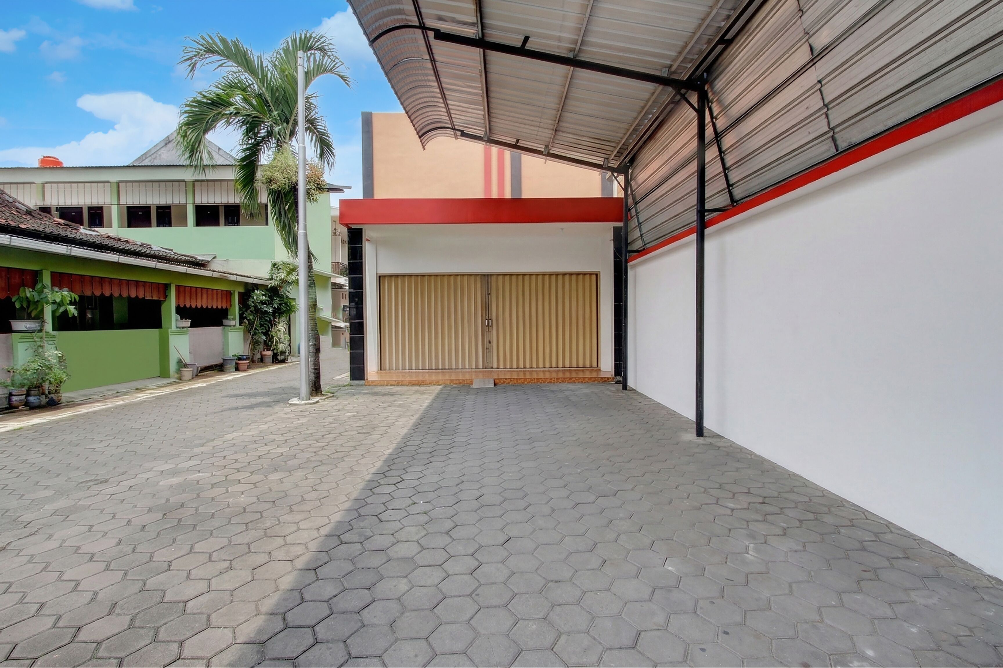 A building with a covered entrance, a tiled walkway, and a palm tree.