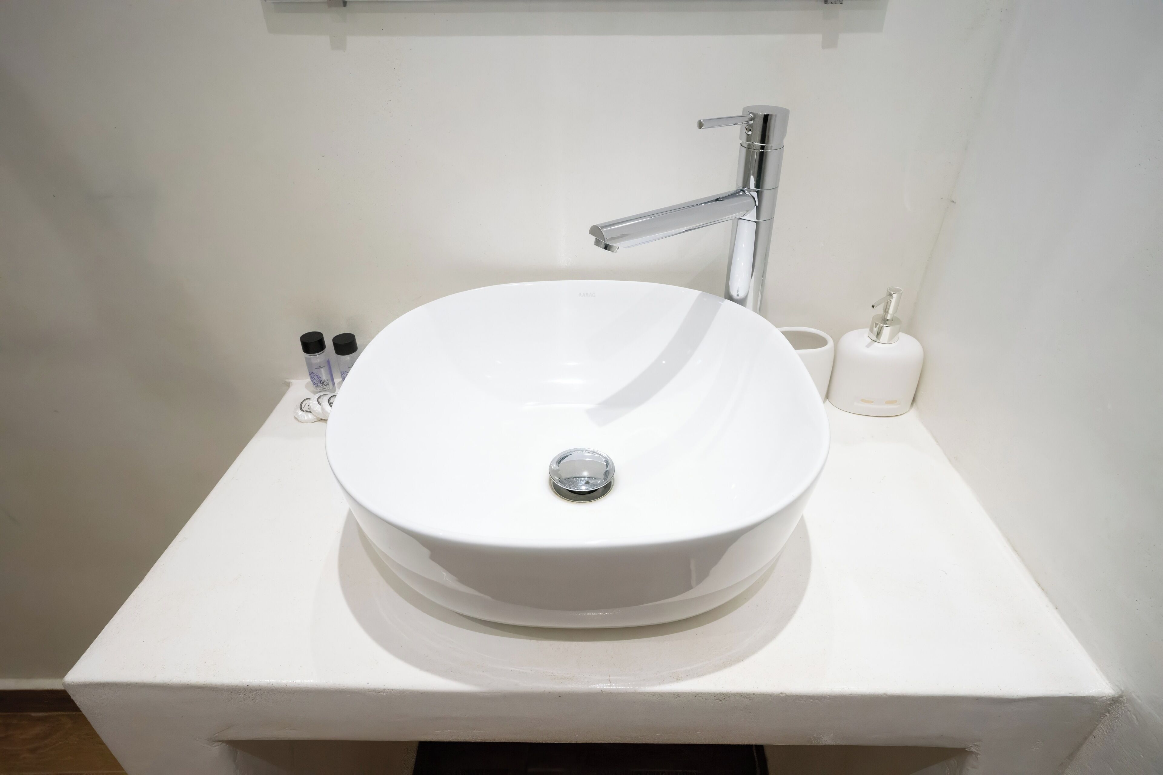 A white bathroom sink with a chrome faucet, a white toilet paper holder, and two small bottles on the counter.