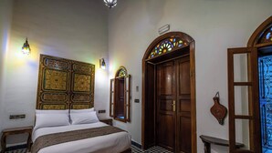 A room with a bed, a wooden door, a wall-mounted mirror, and a patterned rug. - Le Cèdre d'Argent (Fes)