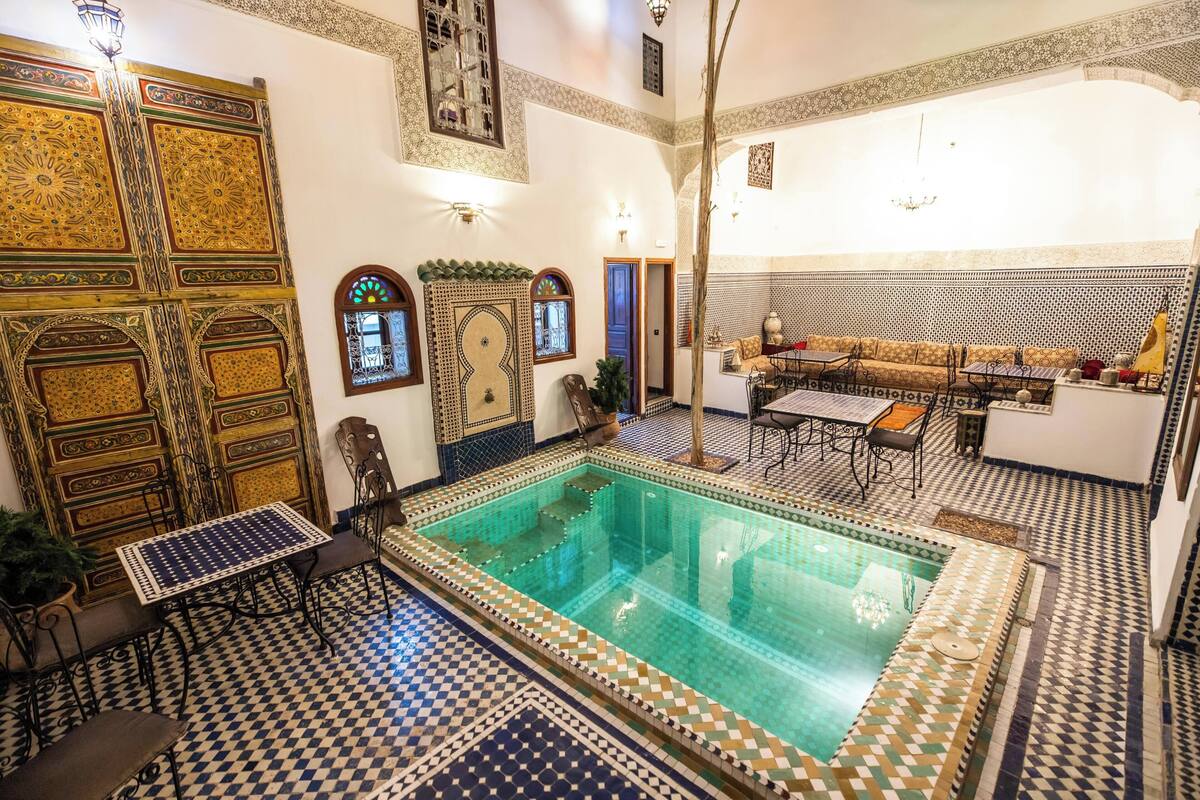 Una piscina interior con suelo de baldosas, una zona de estar con sofá y sillones, y paneles decorativos en las paredes.