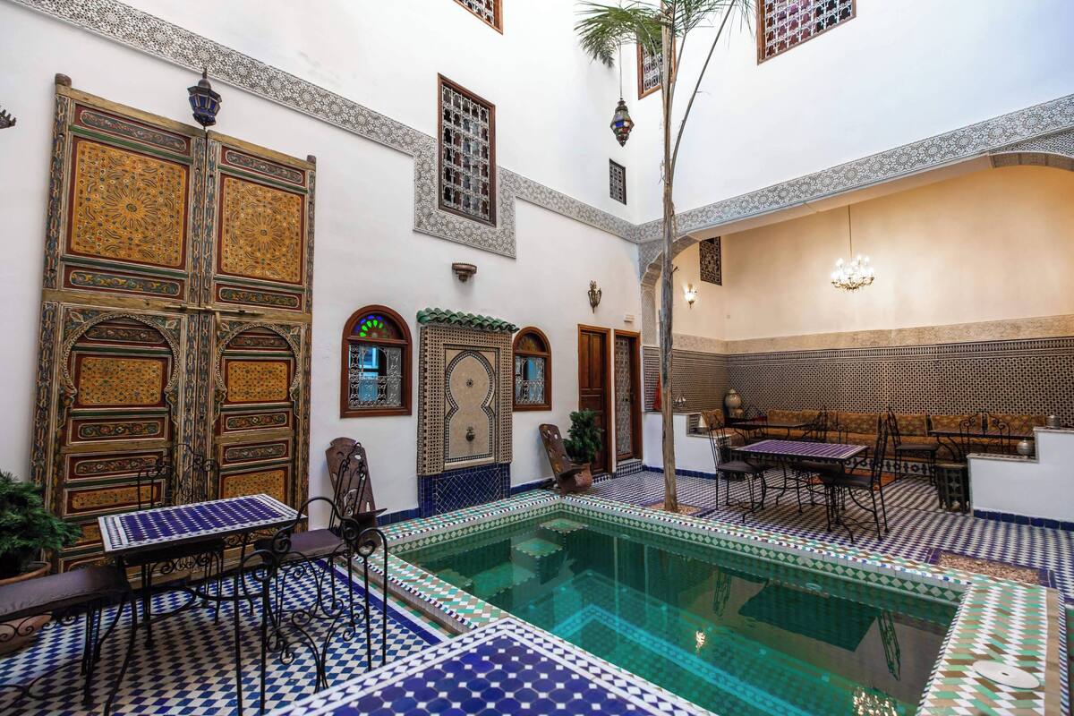 Un patio con piscina, suelo de baldosas y puertas tradicionales marroquíes.