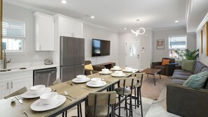 Una cocina moderna con armarios blancos, un refrigerador de acero inoxidable y un comedor con una mesa larga dispuesta para seis personas.