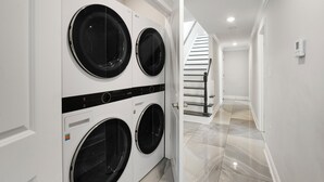 Un lavadero con cuatro lavadoras de carga frontal, una escalera que sube a un piso superior y un suelo limpio con baldosas.