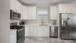 A modern kitchen with white cabinets, stainless steel appliances, and a marble floor. - Remarkable Superdome Group Home w/Heated Pool, Parking, Patio, 8 Beds & 5 Baths (New Orleans)