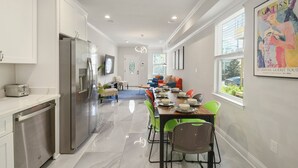 A modern kitchen with stainless steel appliances, a dining area with green chairs, and a living room with a sofa and a TV. - Remarkable Superdome Group Home w/Heated Pool, Parking, Patio, 8 Beds & 5 Baths (New Orleans)