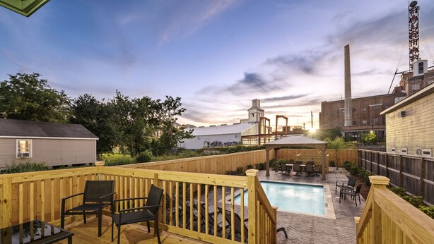 A wooden deck with outdoor furniture, a swimming pool, and a view of an industrial area with buildings and a tall chimney. - Remarkable Superdome Group Home w/Heated Pool, Parking, Patio, 8 Beds & 5 Baths (New Orleans)