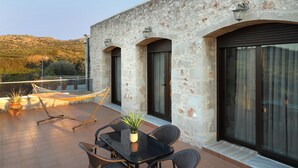 A terrace with a table and chairs, a hammock, and a potted plant. - Heliopetra Lux Villa with private Pool (Chania)