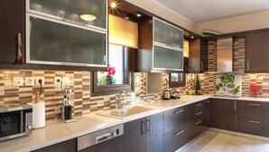 A modern kitchen with dark cabinetry, a double sink, and a built-in microwave. - Heliopetra Lux Villa with private Pool (Chania)