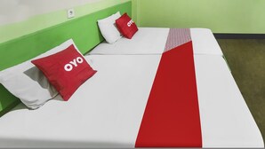 Ein Bett mit weißroter Bettdecke, zwei rote Kissen mit dem Aufdruck "OYO" und ein grünes Kopfteil.