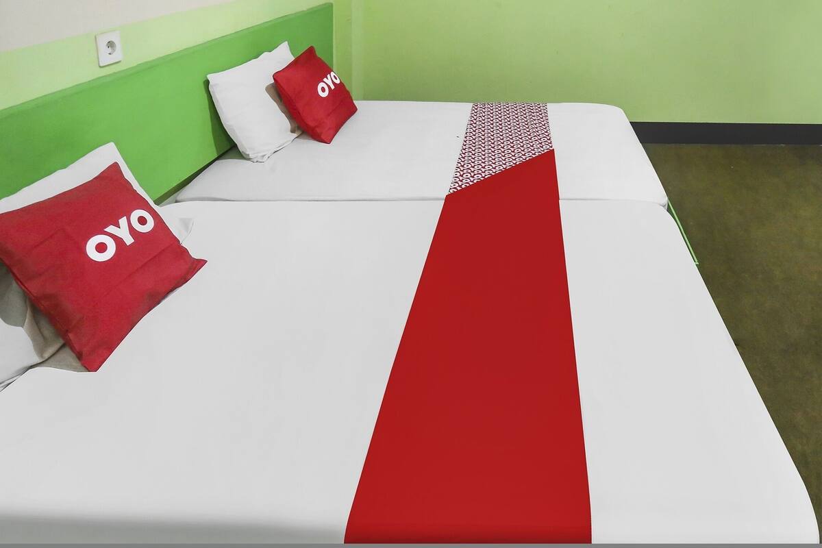 Una cama con una colcha blanca y roja, dos almohadas rojas con el texto "OYO" y un cabecero verde.