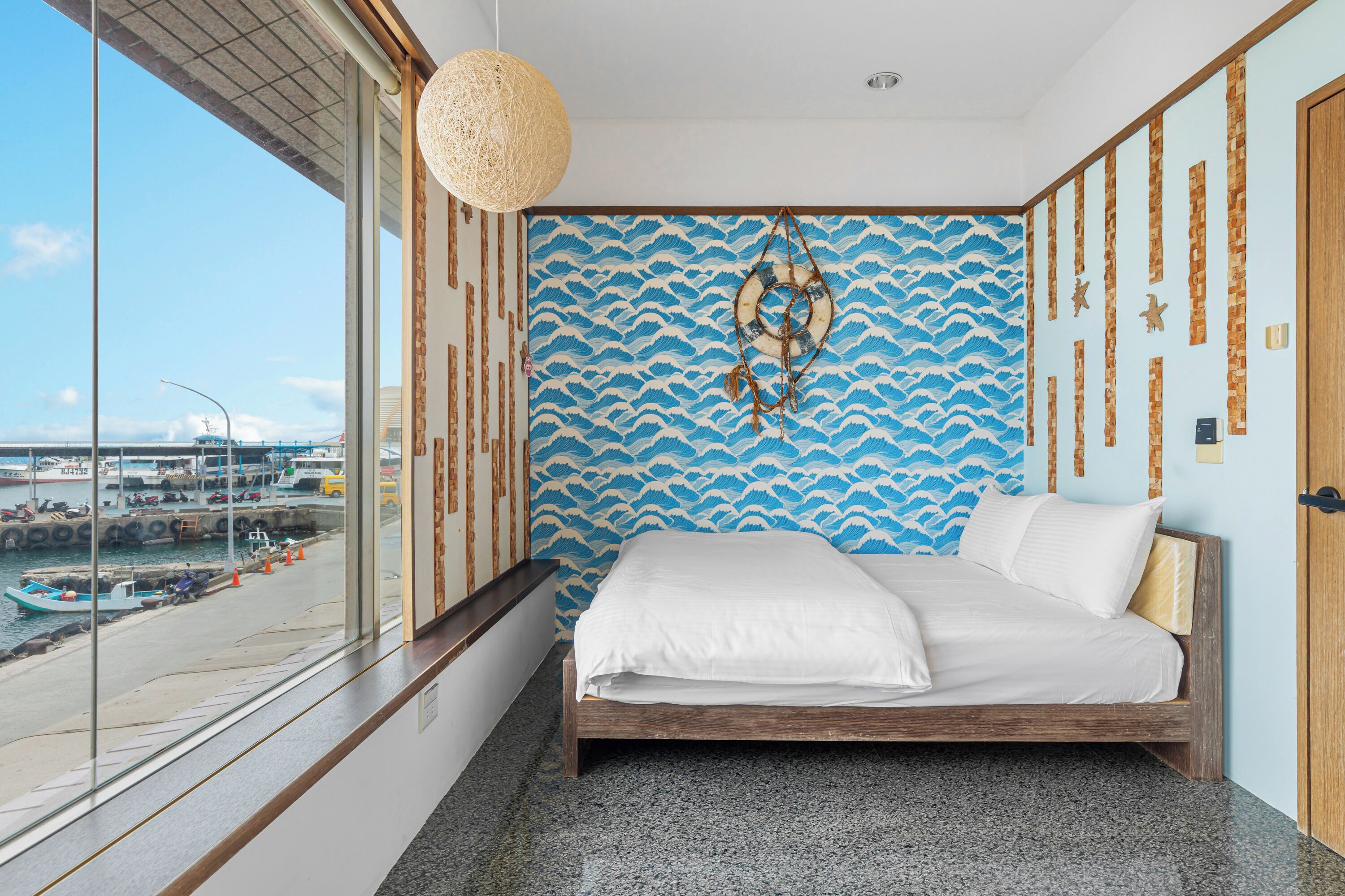 Een slaapkamer met een groot raam, een bed en uitzicht op een haven.