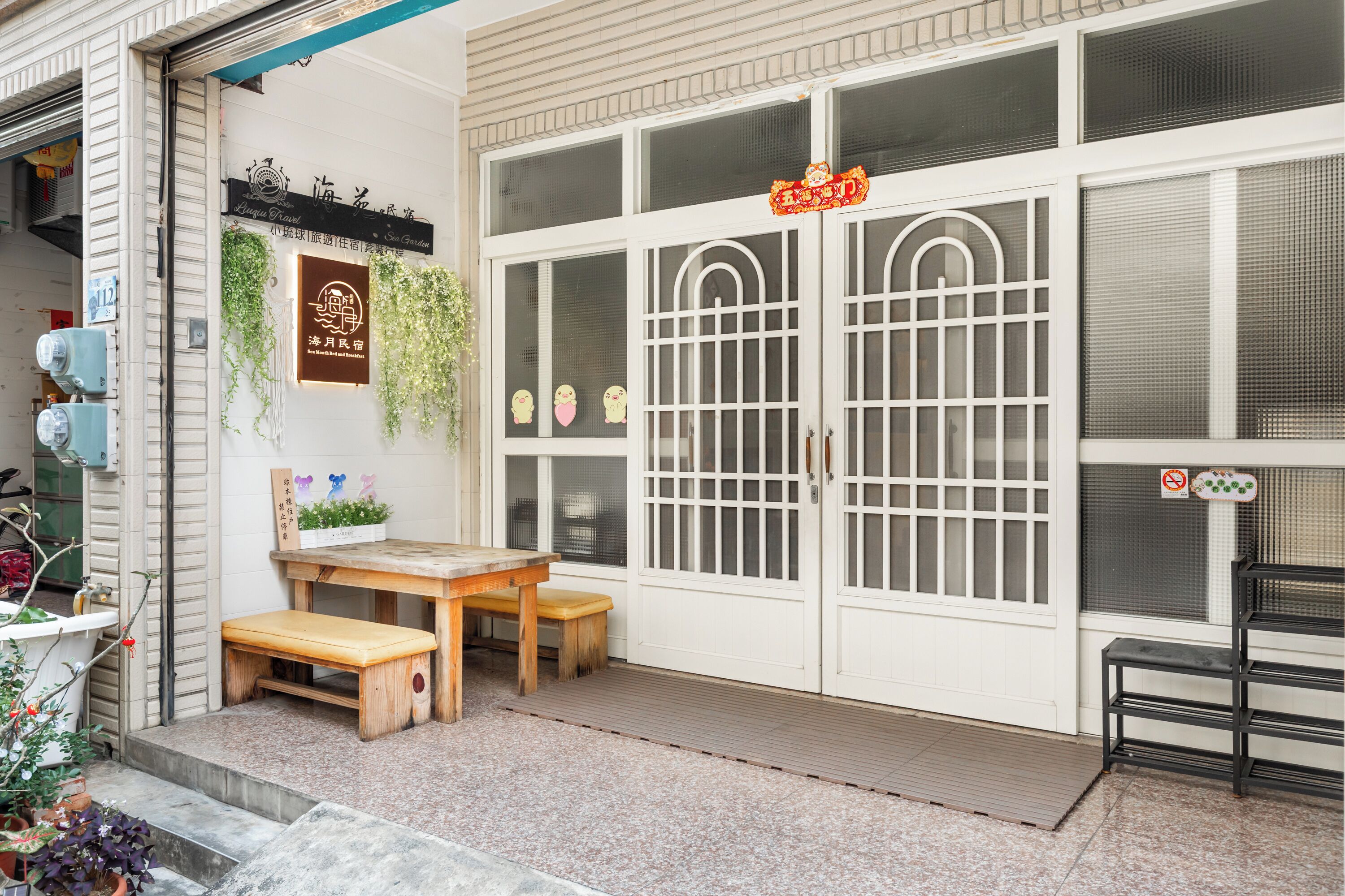 A traditional Japanese-style entrance with a wooden bench, a small table, and a decorative sign above the door.