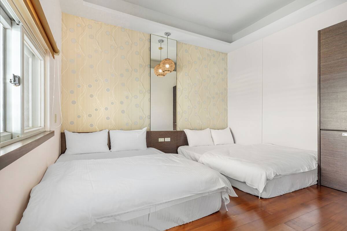 A hotel room with two beds, a large mirror, and a window with blinds.